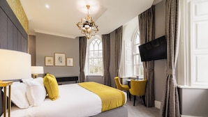 A hotel room with a bed, a desk, a chair, a television, and a window with curtains. - Vale Resort (Pontyclun)