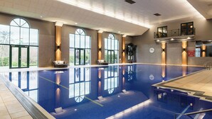 A large indoor swimming pool with clear glass walls, a reception area, and a staircase leading to an upper level. - Vale Resort (Pontyclun)