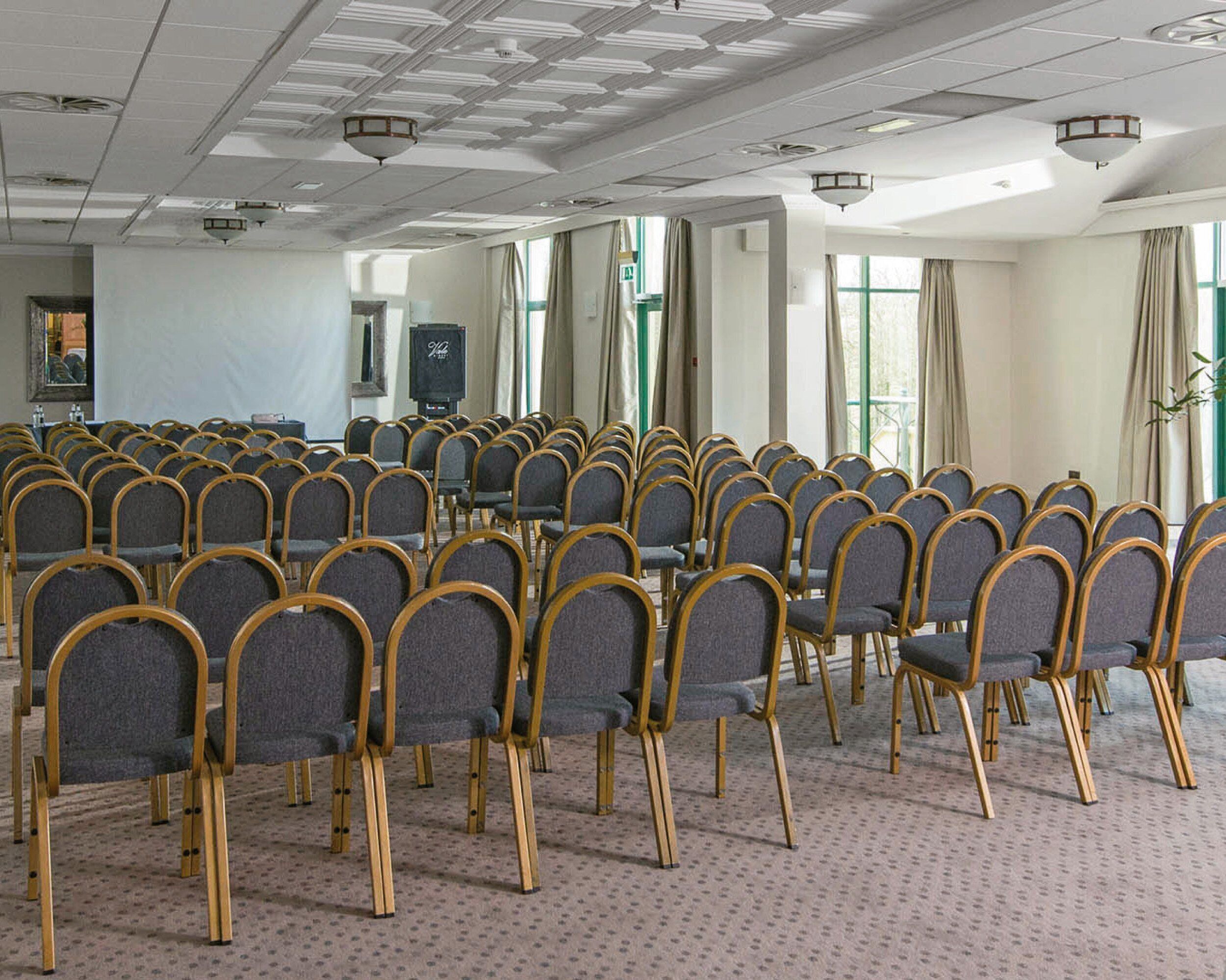 A conference room with rows of chairs, a carpeted floor, and large windows with curtains.