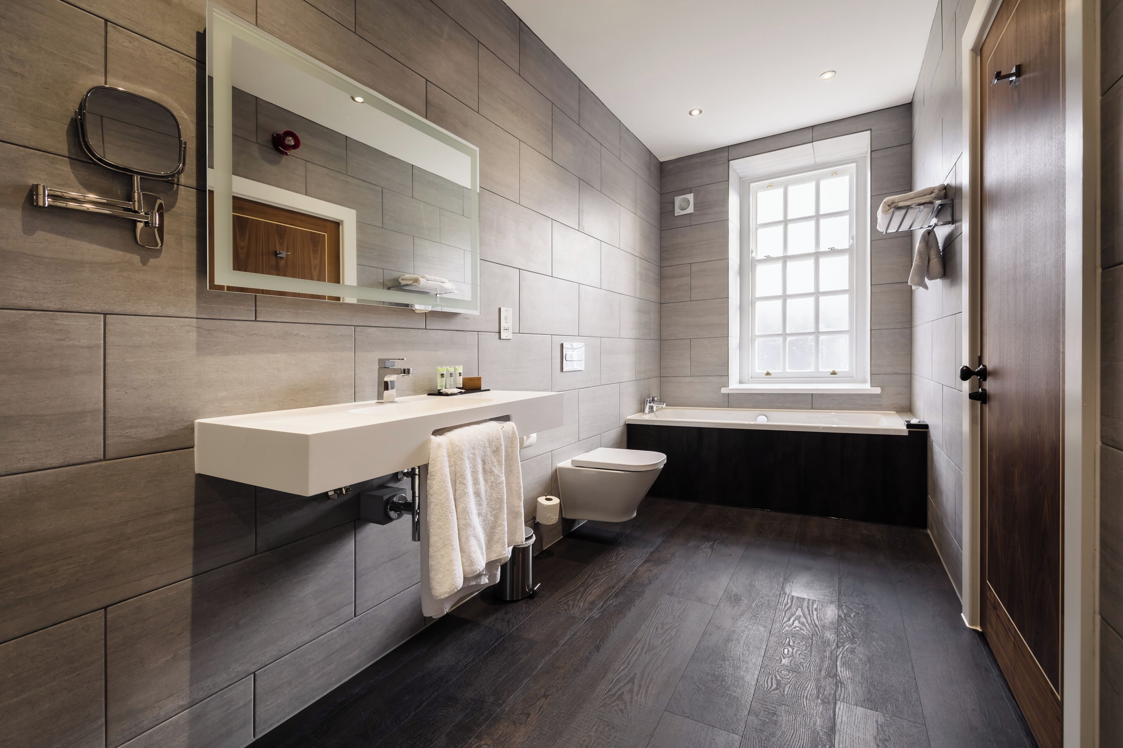 Ein modernes Badezimmer mit einem großen Spiegel, einer Toilette, einer Badewanne und einem Fenster.