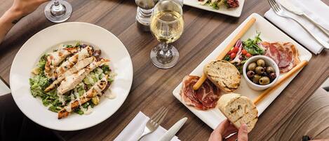 Une table à manger dressée avec différents plats, notamment une salade, du poulet grillé et du pain, ainsi que des verres à vin et des couverts.