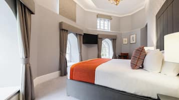 A modern hotel room with a large bed, a flat-screen TV, a window with curtains, and a chandelier.