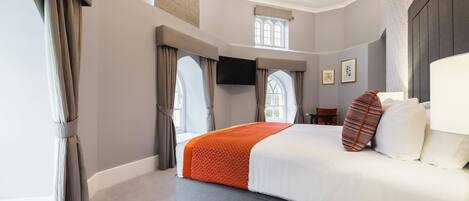 A modern hotel room with a large bed, a flat-screen TV, a window with curtains, and a chandelier.