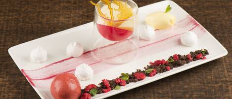 Un plato de postre con varios elementos, incluyendo un vaso con líquido rojo, una bola de helado y adornos como frambuesas y hojas de menta.