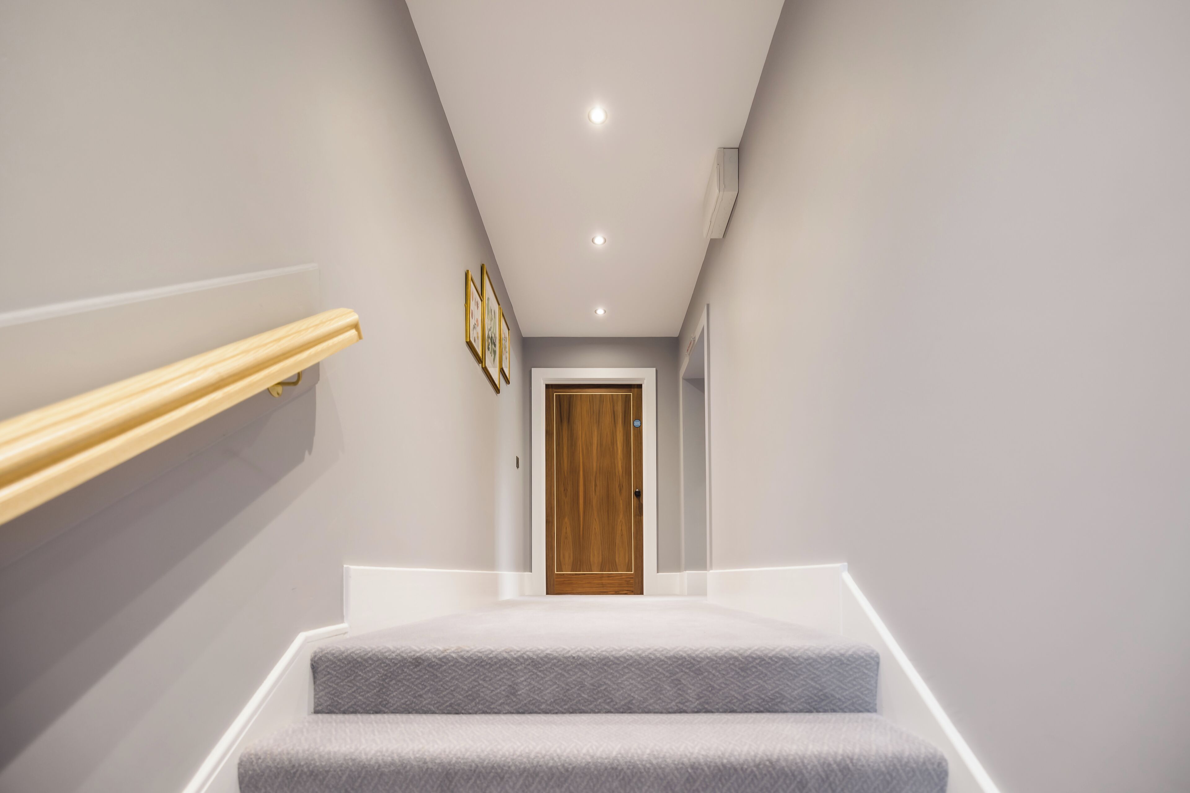 Eine moderne Treppe mit Holzwandhandlauf und einem grauen Teppichpodest.