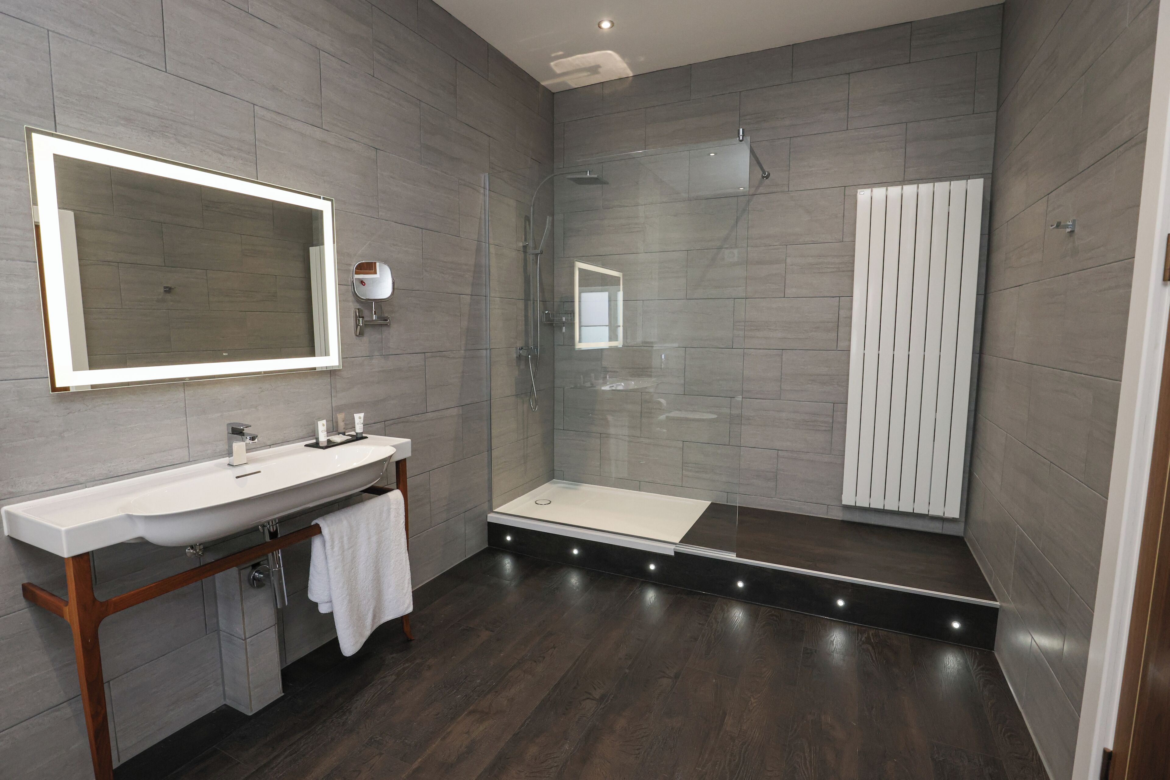 A modern bathroom with a large mirror, a vanity with a sink, and a shower area.