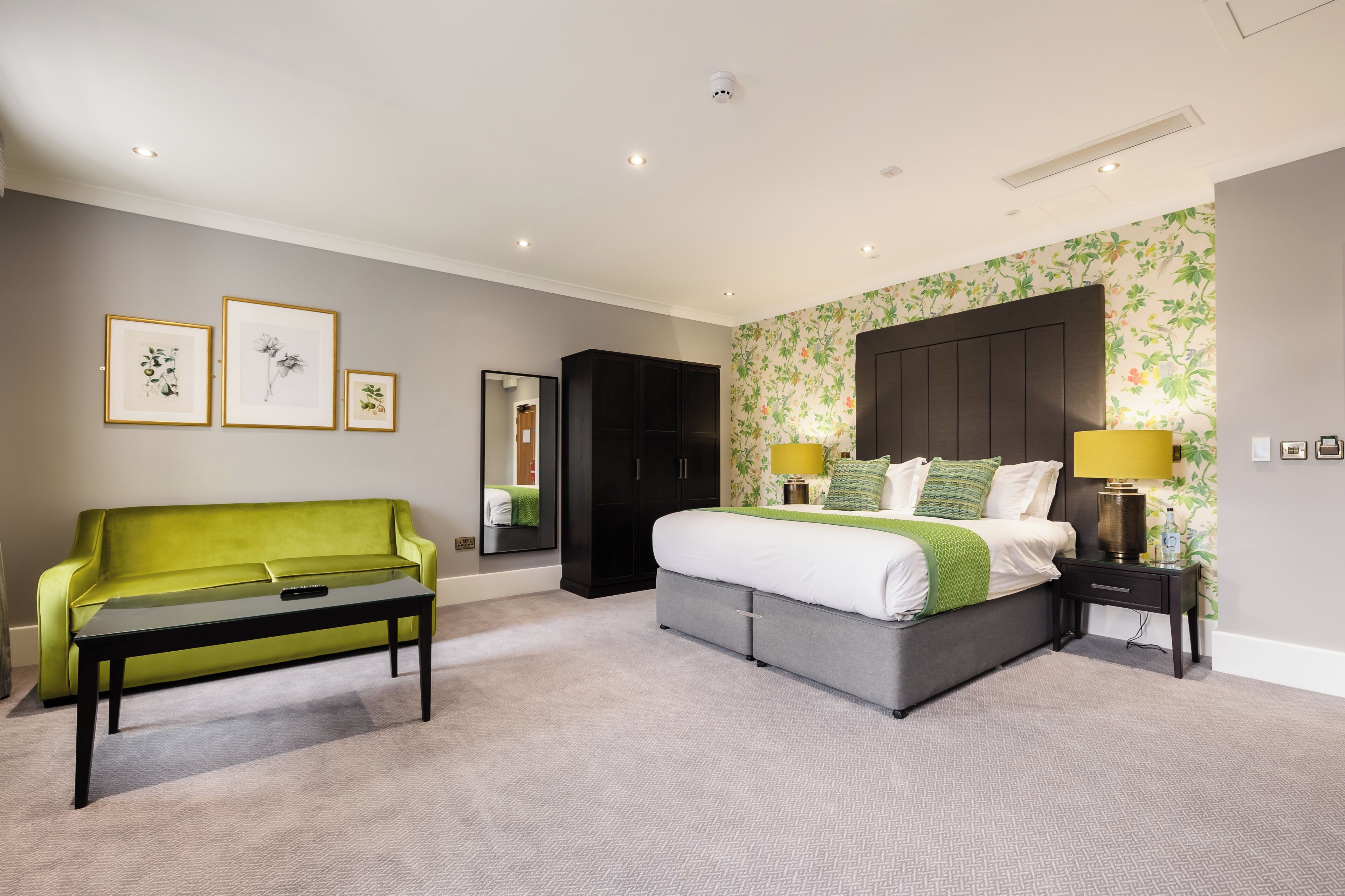 A bedroom with a bed, bedside table, lamp, and a green sofa.