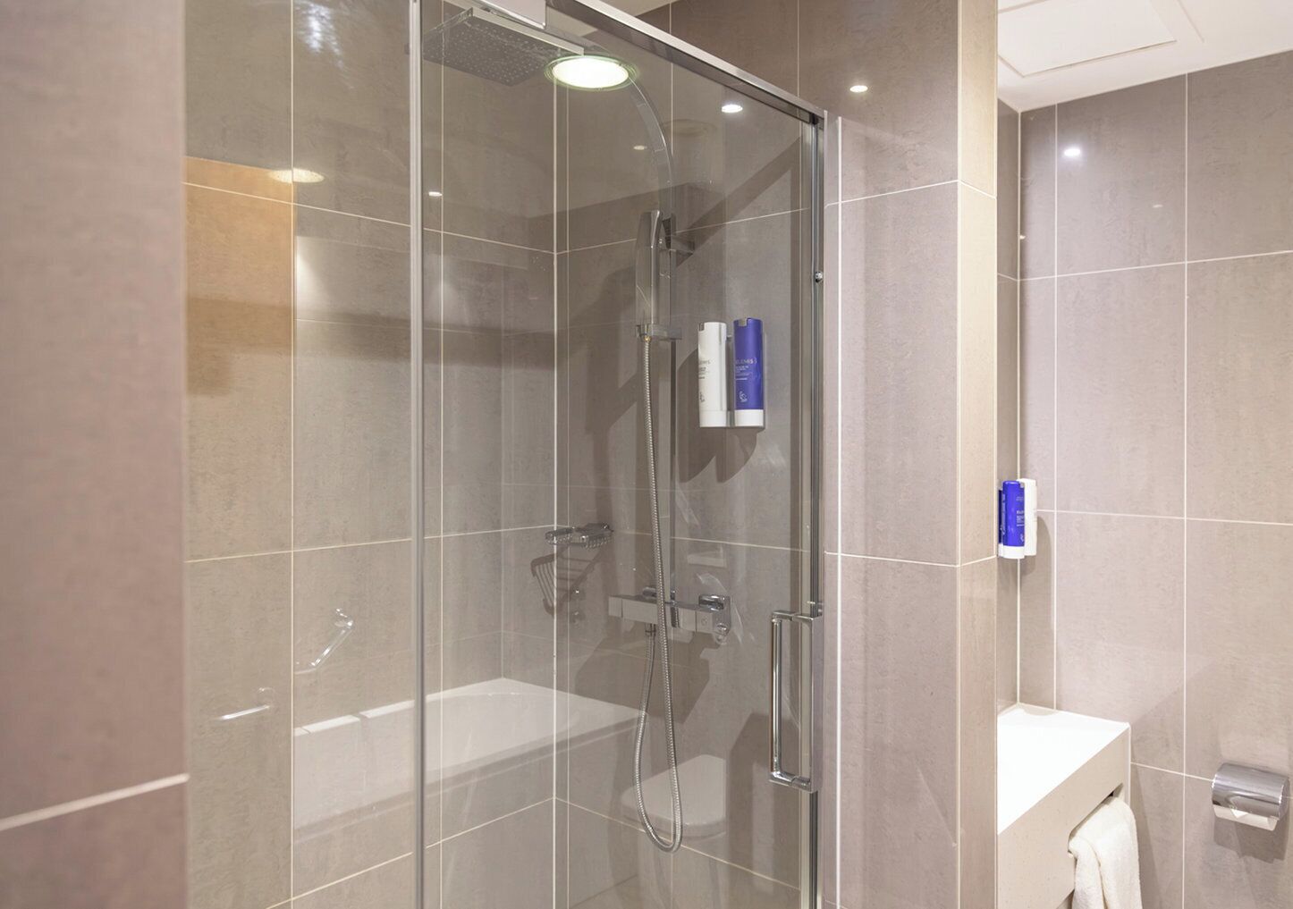 A modern bathroom with a glass-enclosed shower, a white sink, and a towel rack.