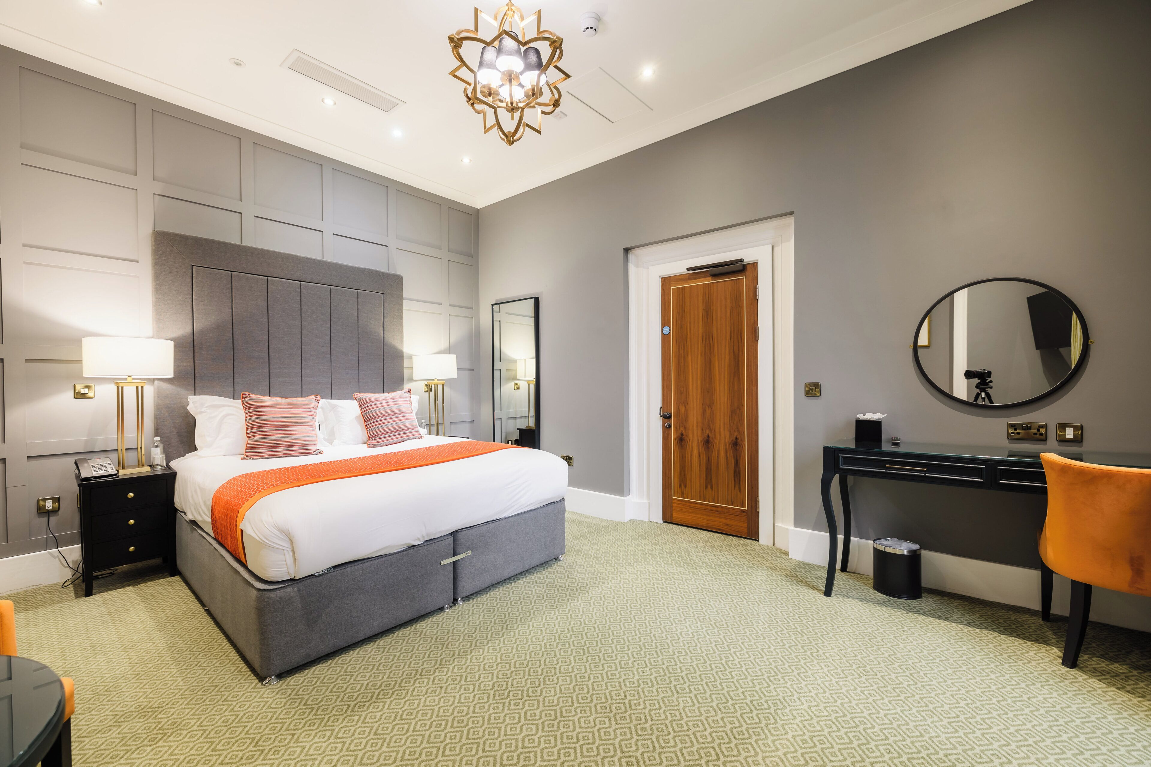 Una habitación de hotel moderna con una cama grande, lámparas de noche, un escritorio, una silla y un espejo.