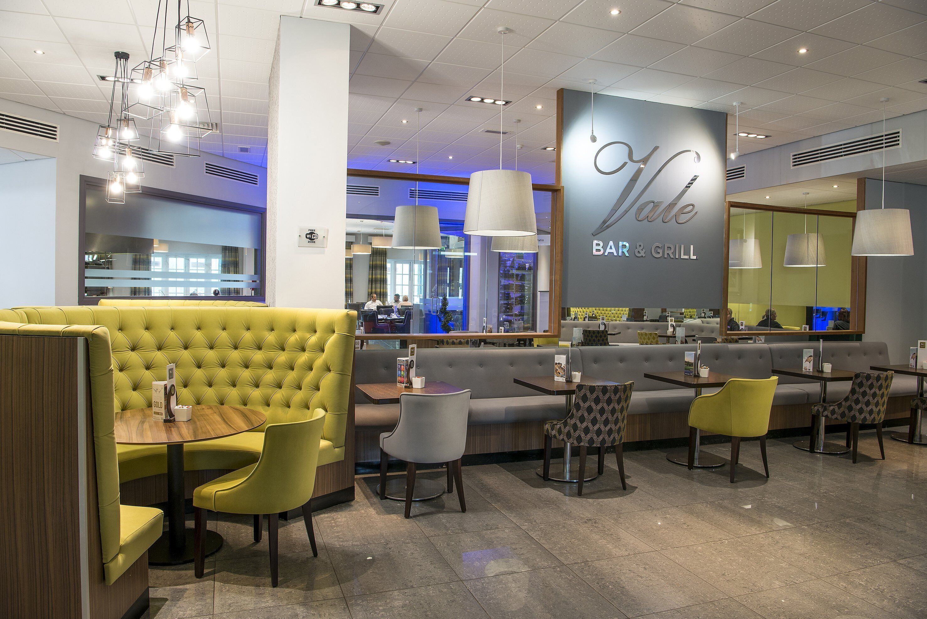 A restaurant interior with yellow booths, grey and yellow chairs, and a bar area.