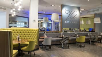 A restaurant interior with yellow booths, grey and yellow chairs, and a bar area.