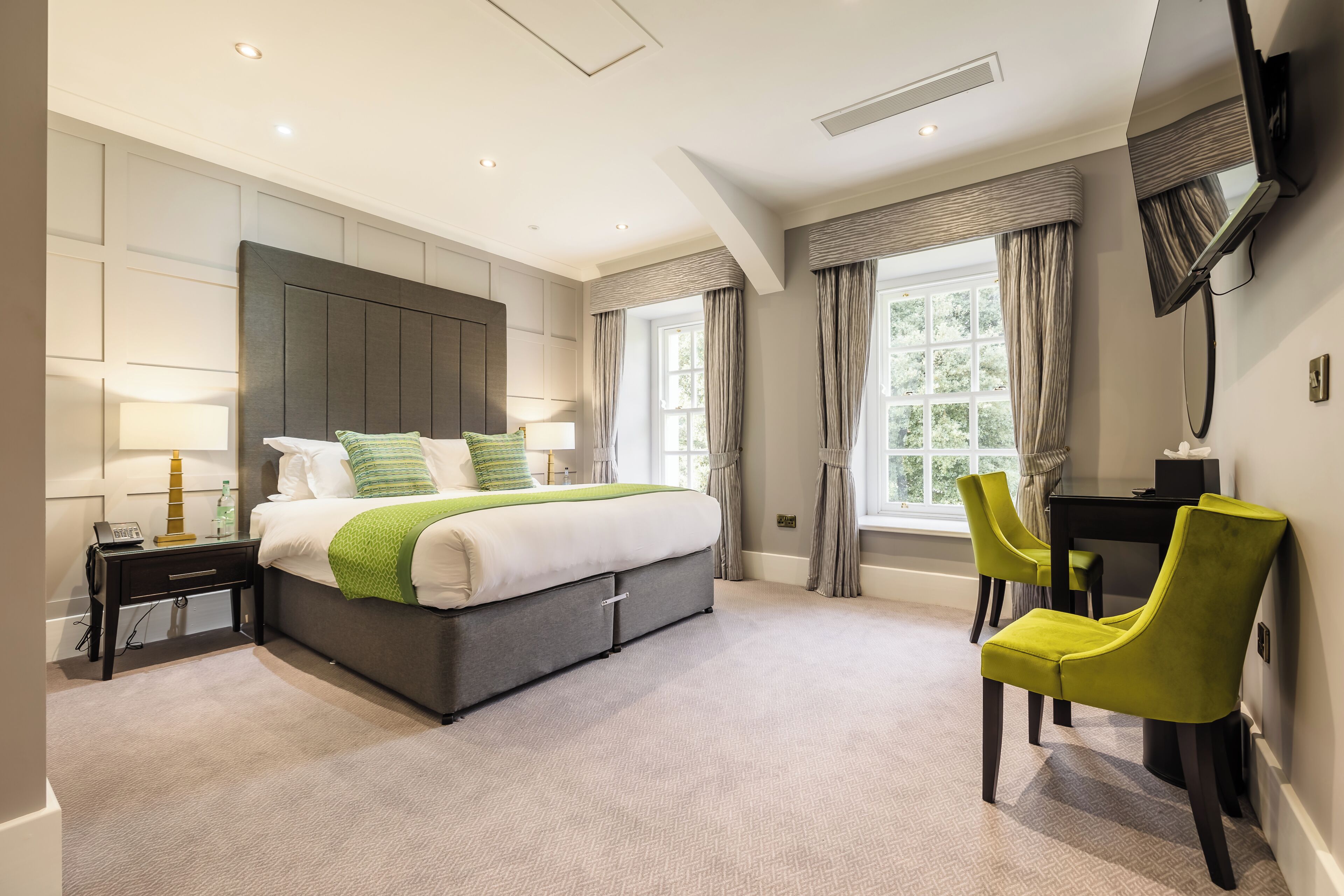 A modern bedroom with a large bed, bedside tables, a desk, and chairs.