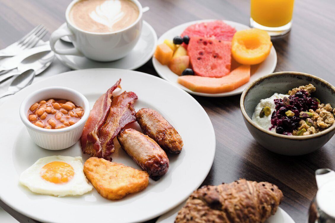 Une assiette de petit-déjeuner comprenant du bacon, des saucisses, des œufs, des toasts et des haricots.