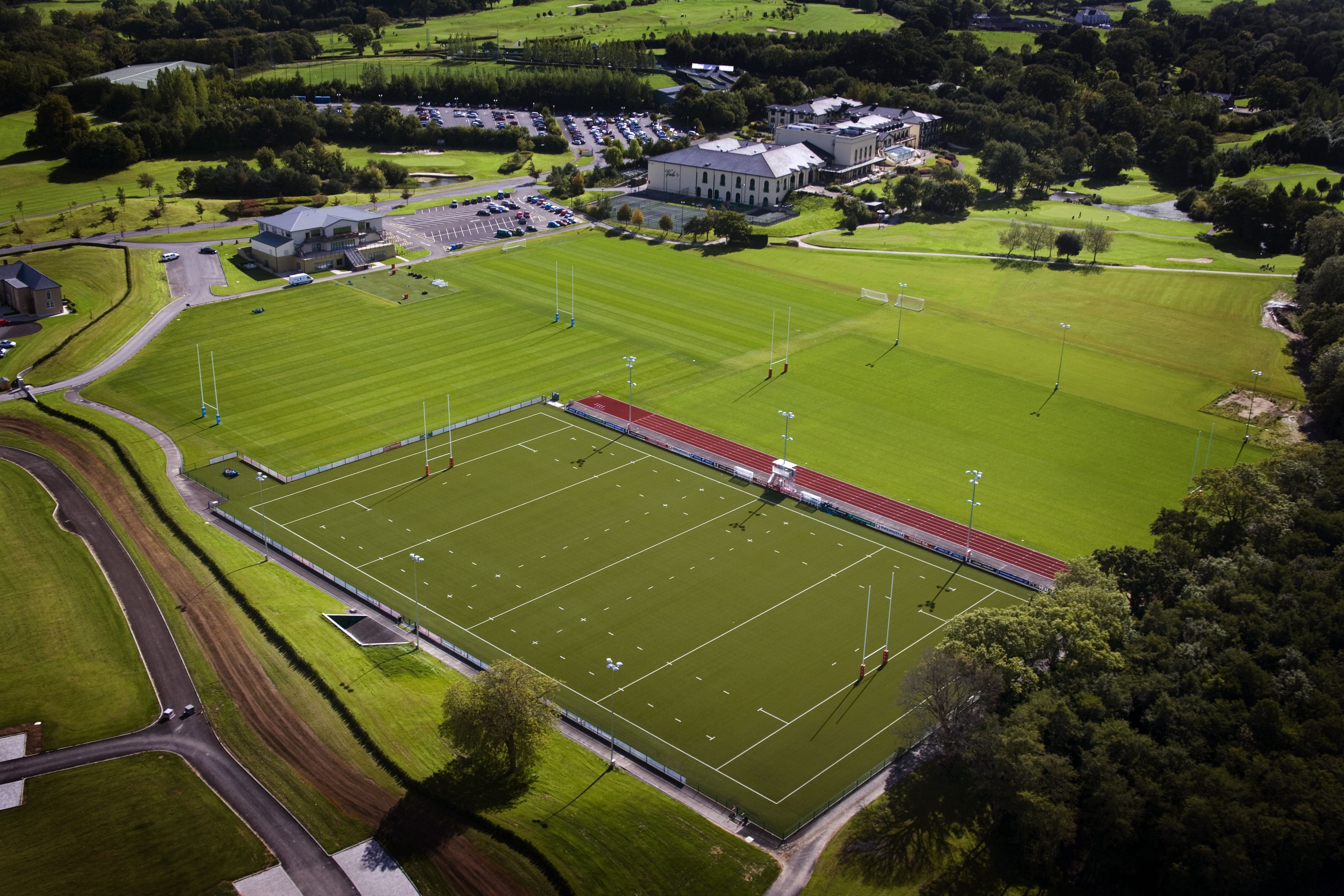 An aerial view of a large sports complex with multiple fields, a running track, and surrounding buildings.