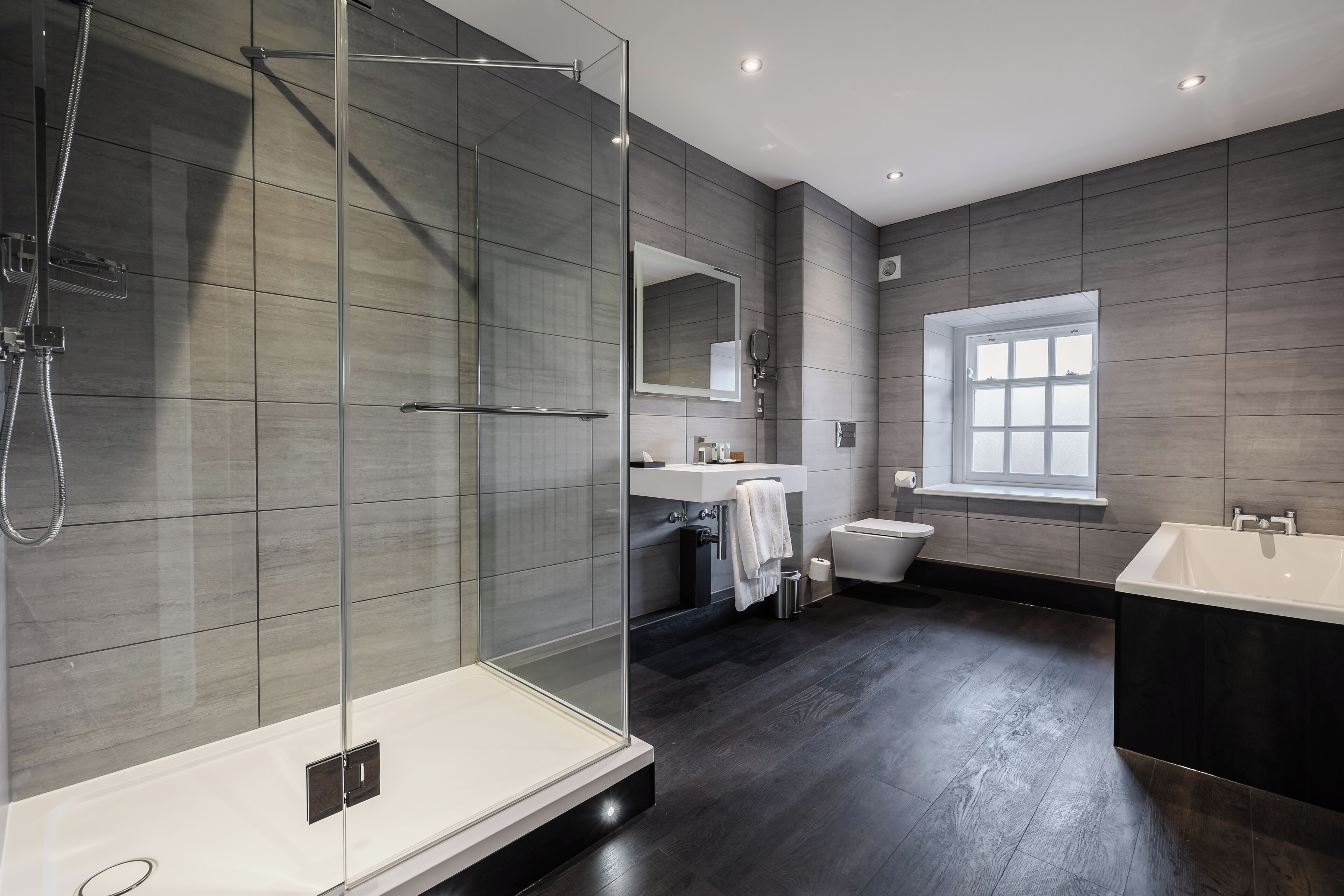 A modern bathroom with a glass-enclosed shower, a large mirror, a bathtub, and a window.
