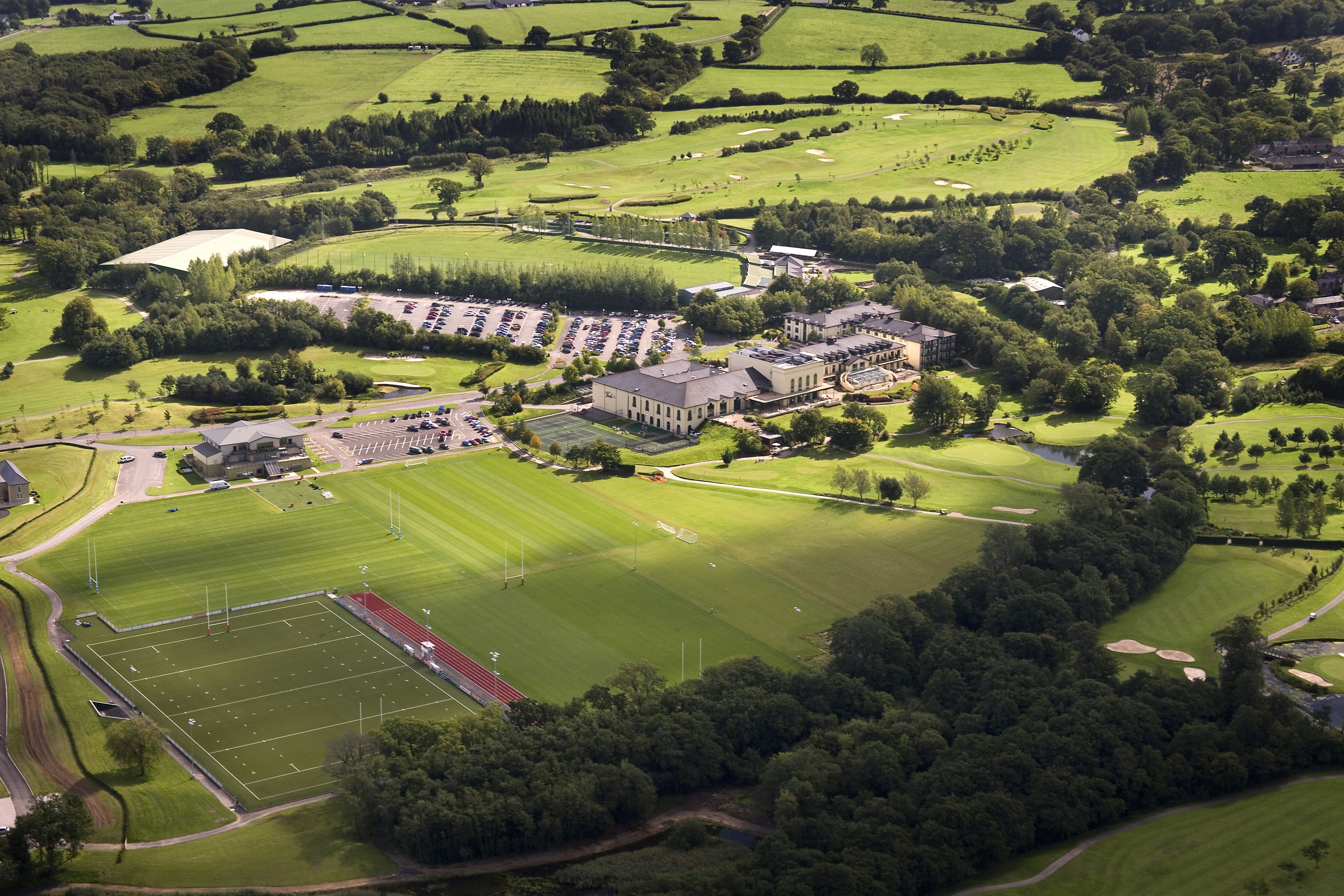Vista aerea di un campo da golf con un ampio club house, un'area di parcheggio e un campo sportivo.