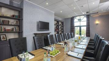 A conference room with a long table, chairs, bookshelves, a fireplace, and a TV.