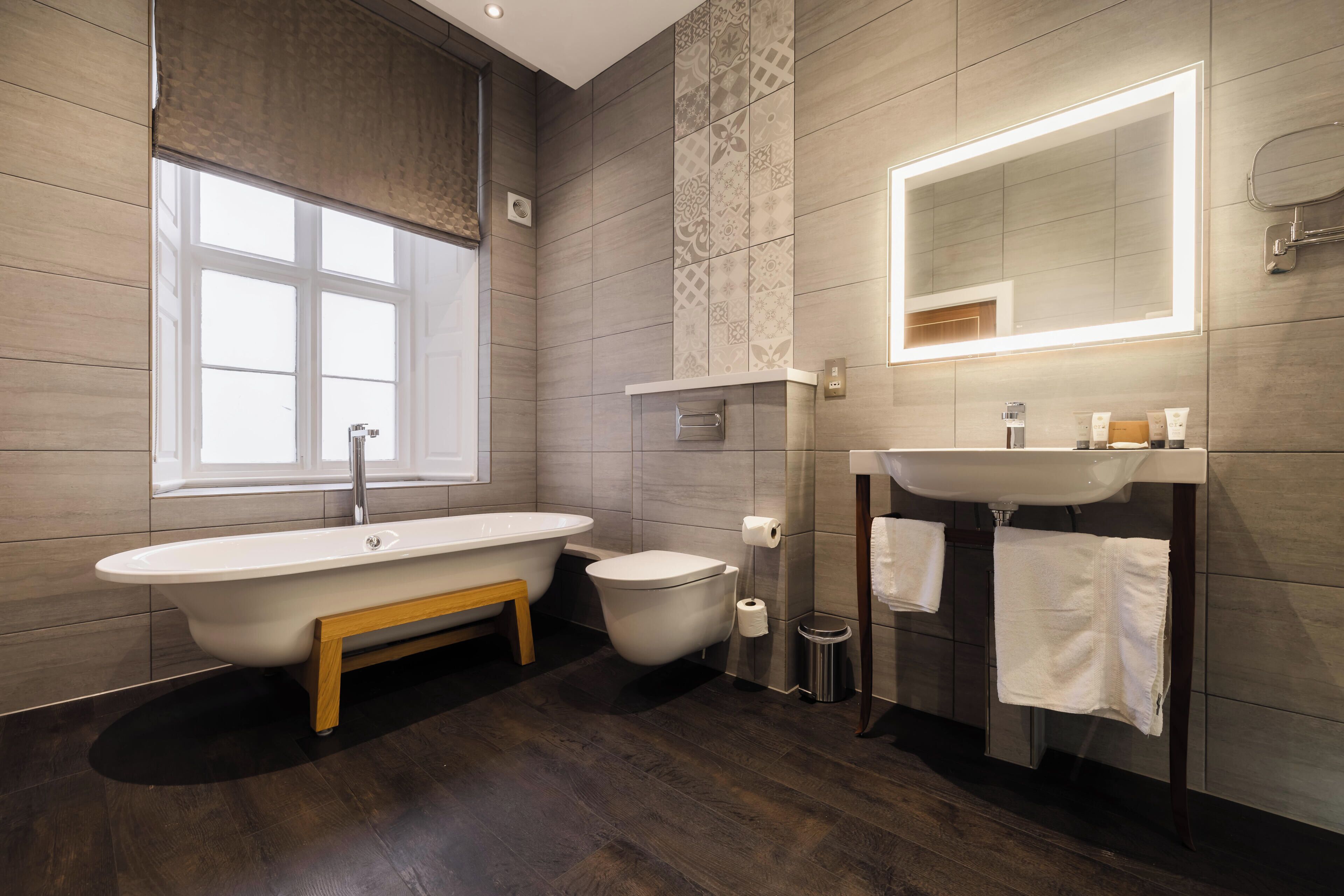 A modern bathroom with a freestanding bathtub, a toilet, a sink with a mirror, and a window.
