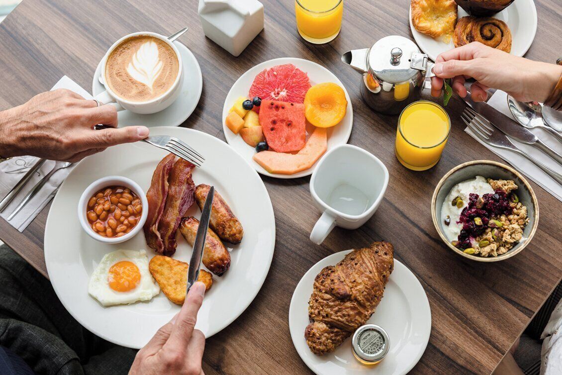 A breakfast setting with various food items and a coffee cup on a wooden table.