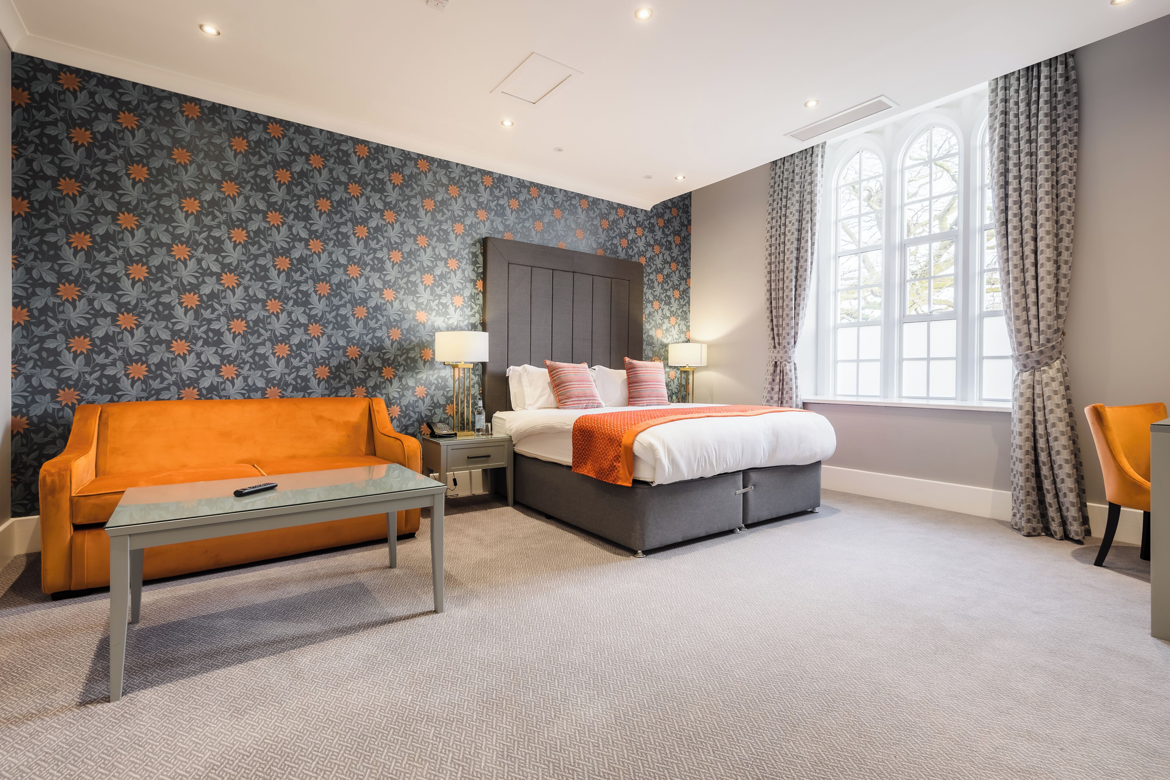A hotel room with a bed, a sofa, a table, and a window with curtains.