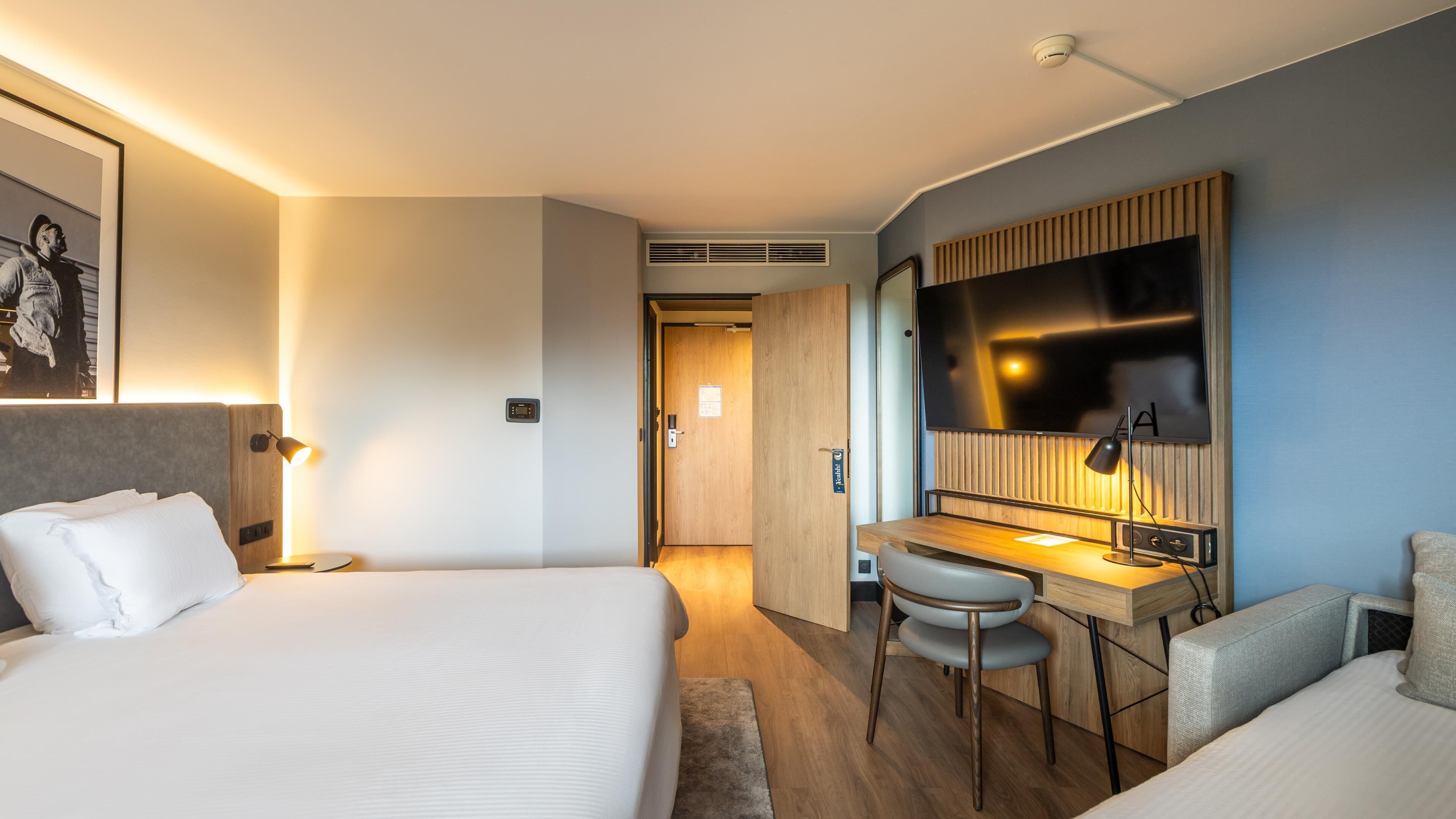 Habitación de hotel con cama, escritorio, silla, televisión y un cuadro en la pared.