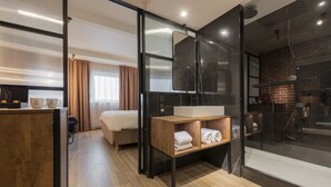 Una habitación de hotel moderna con una cama, un tocador de madera con espejo, un lavabo y una zona de ducha.