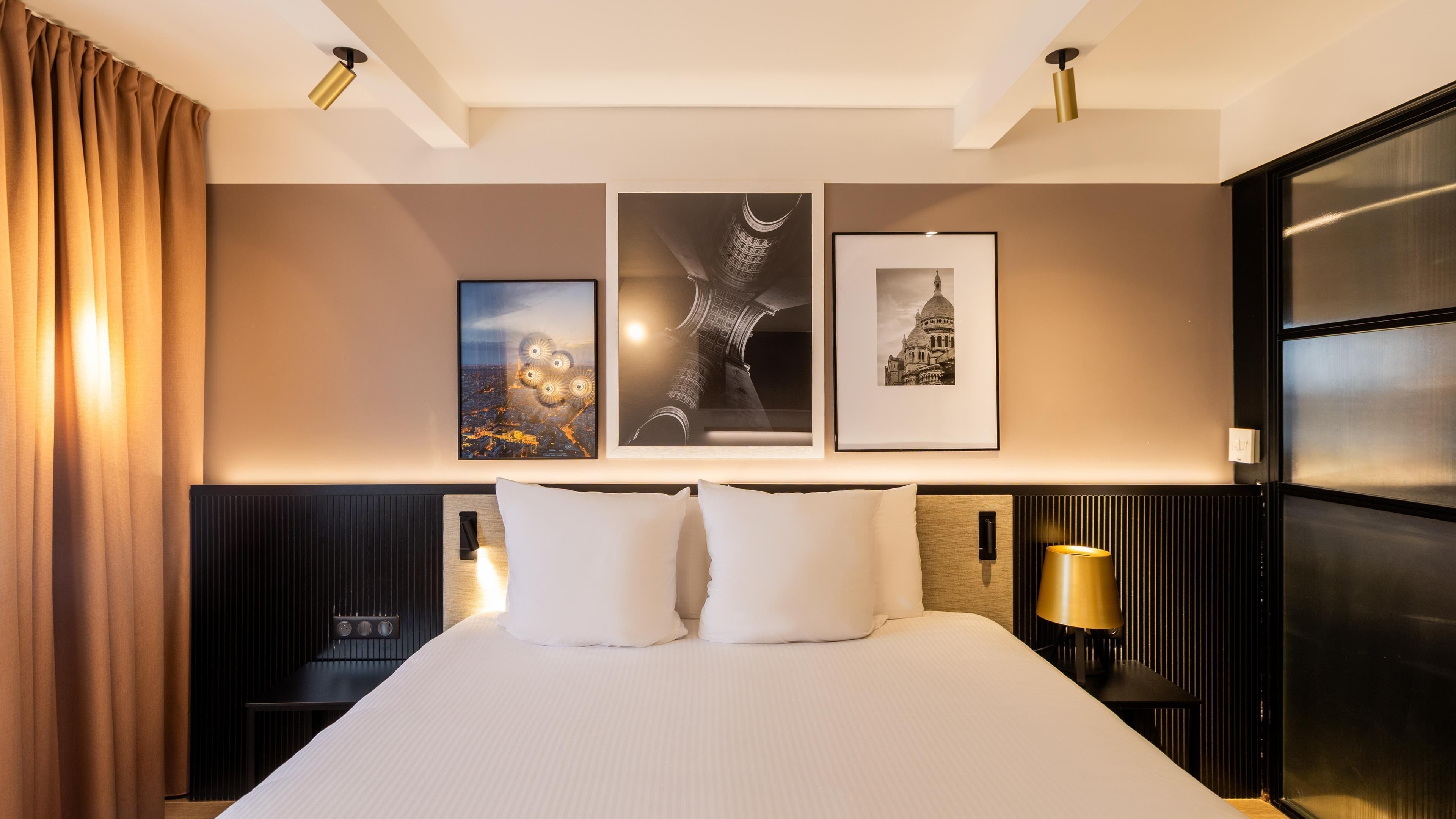 A hotel room with a large bed, two bedside tables, a headboard, and wall-mounted artwork.