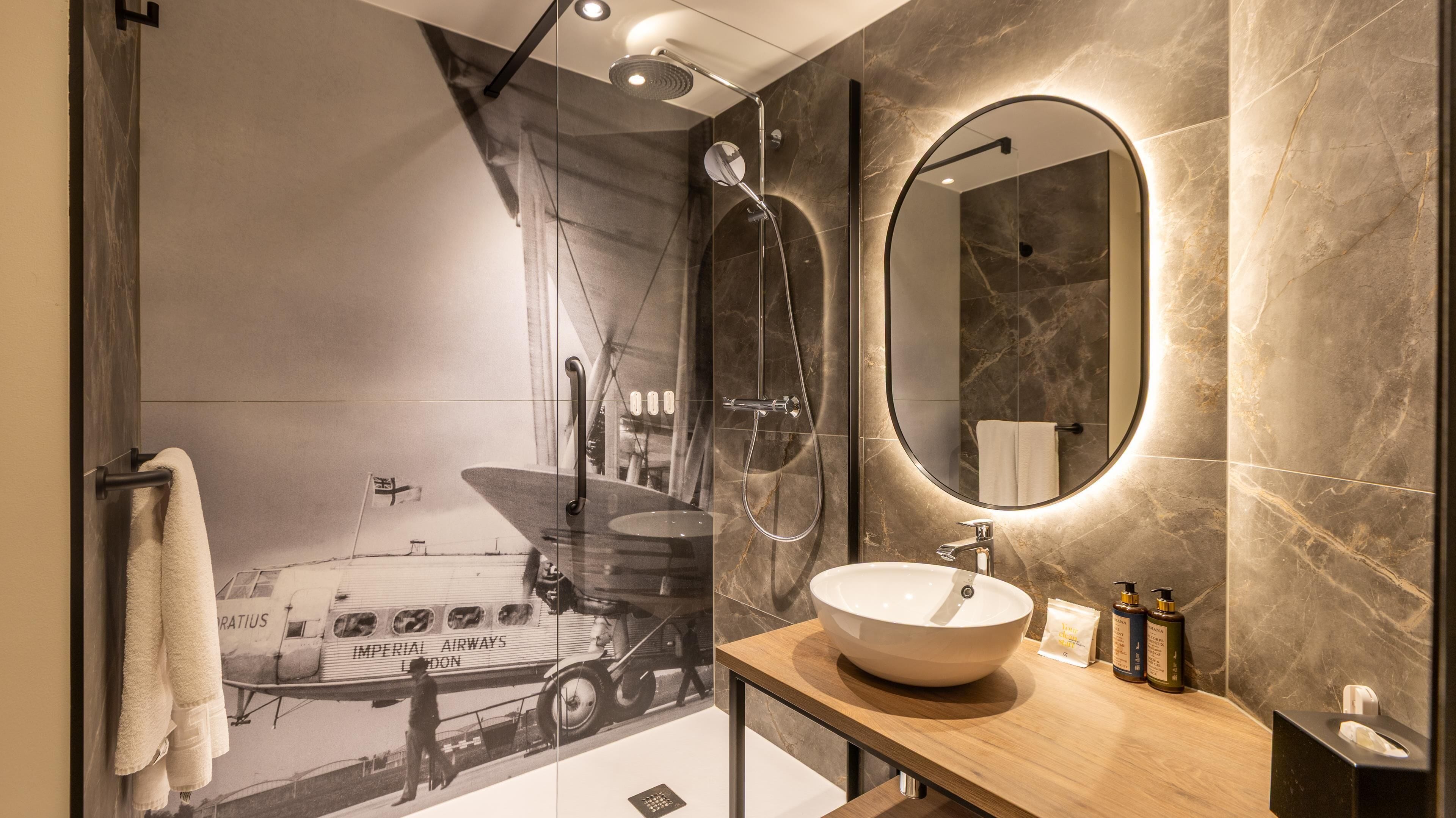 A modern bathroom with a large mirror, a round sink, and a shower with a glass door.