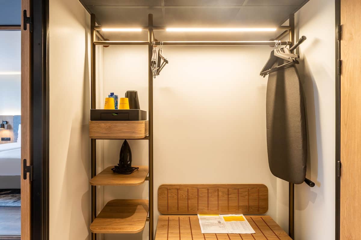 Et lille værelse med seng, et lille træbord, en hylde med toiletartikler og et ophængt tøj.