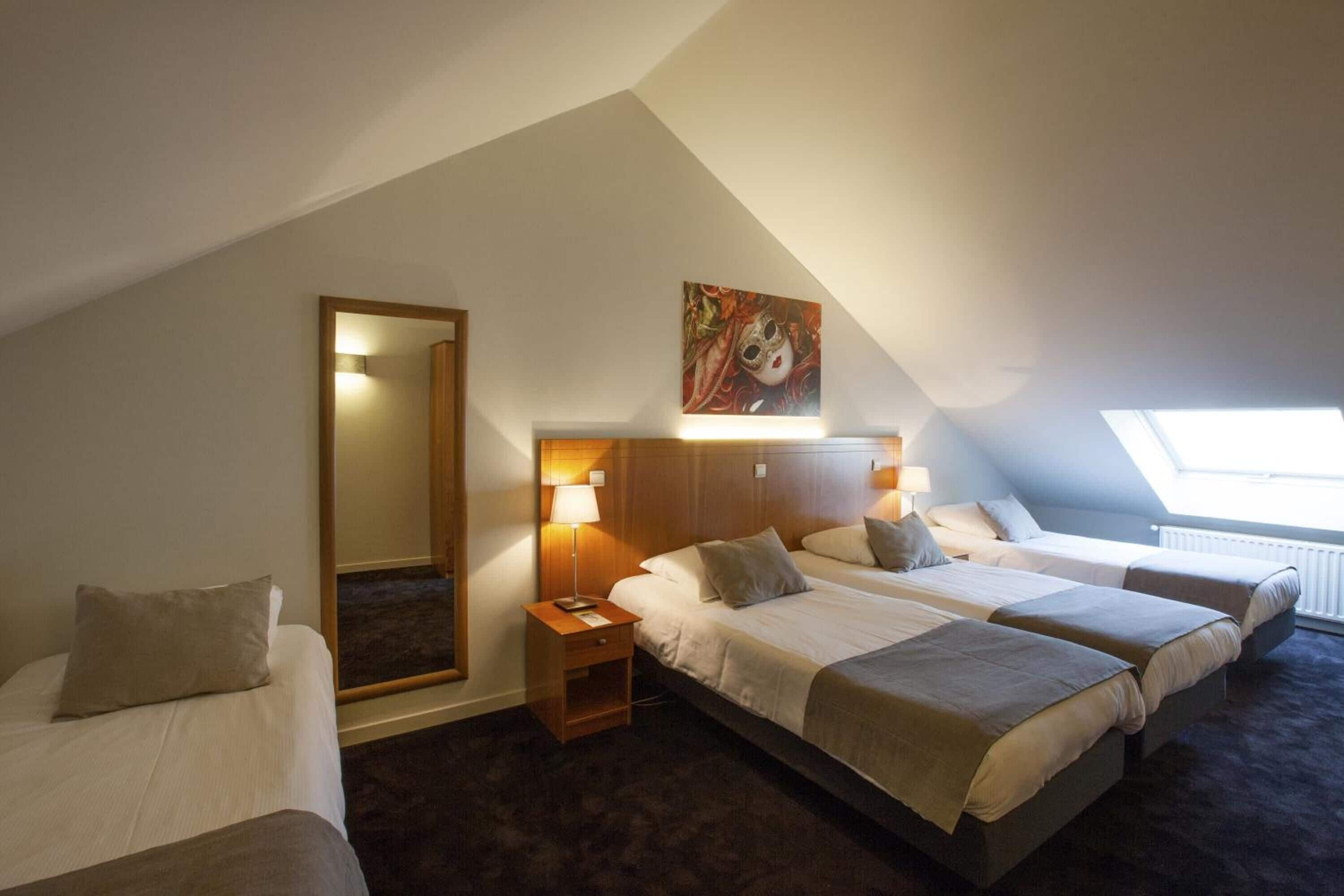Habitación de hotel con dos camas, un espejo grande y un tragaluz.