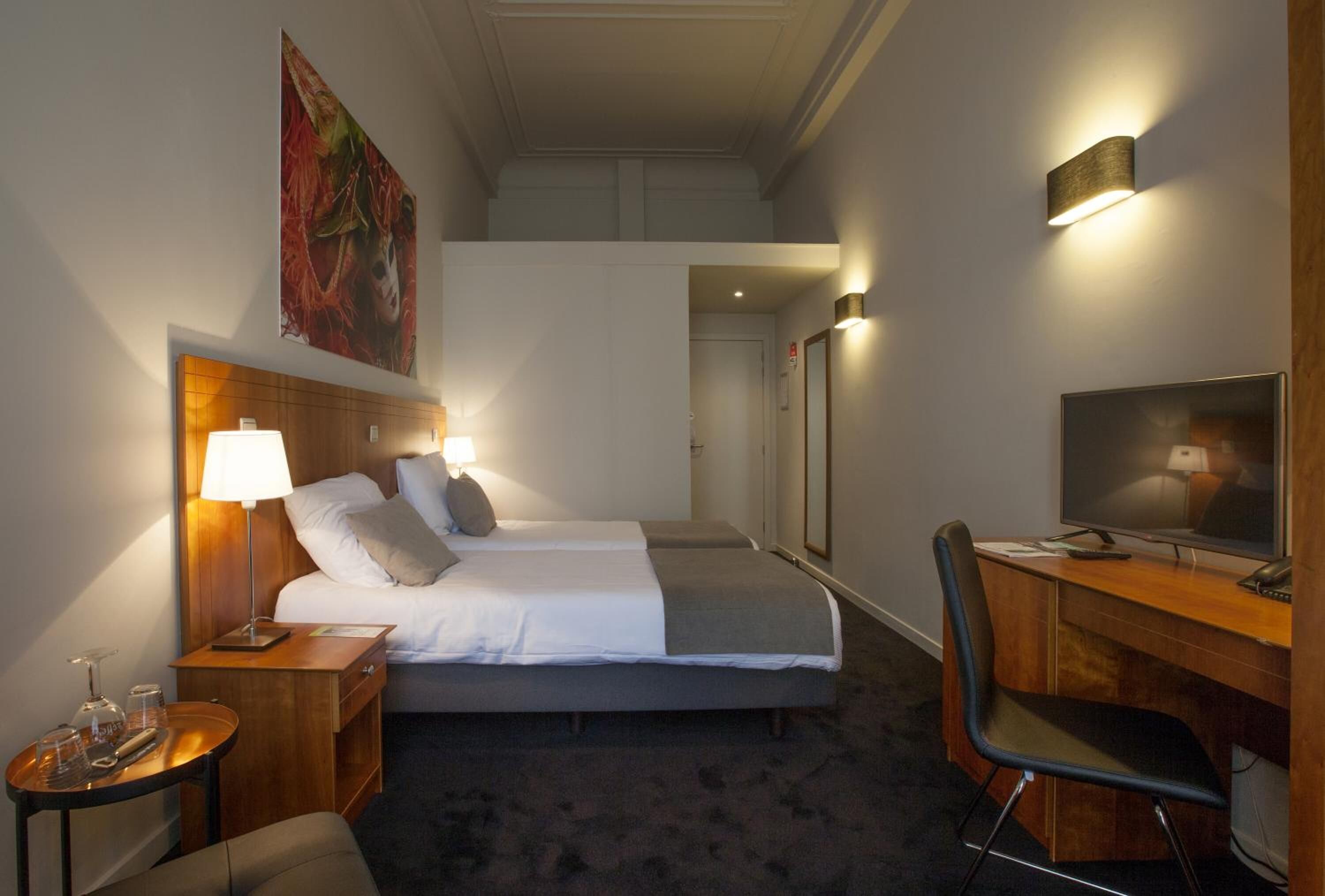 A hotel room with a bed, bedside table, lamp, desk, chair, and a television.