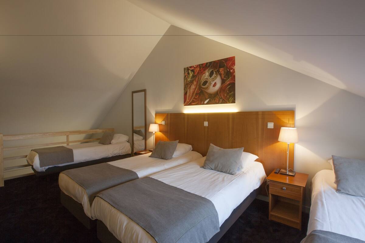 Una habitación de hotel con dos camas, cabecero de madera, lámparas de noche y un cuadro en la pared.