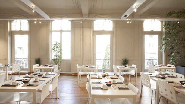 Un comedor espacioso con múltiples mesas y sillas, ventanas amplias y un balcón con plantas.