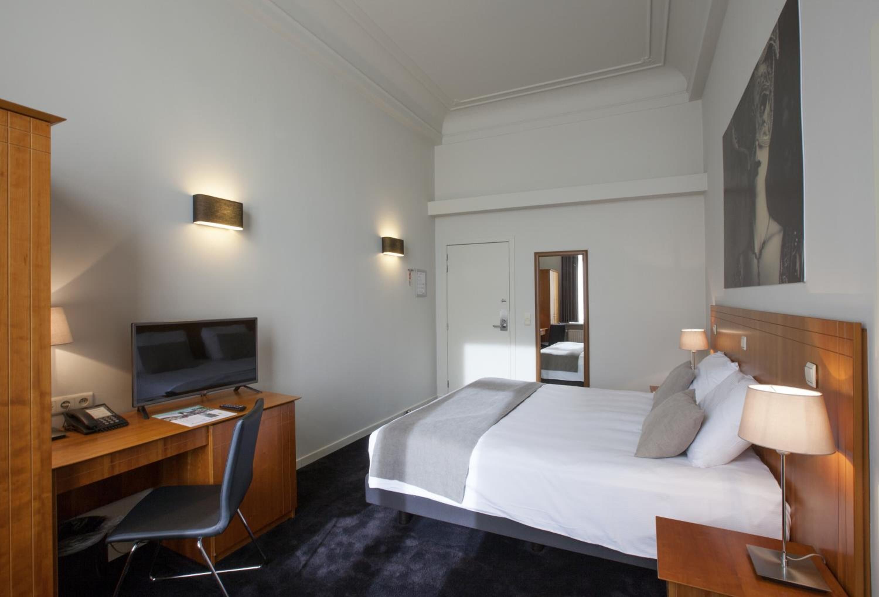 Ein Hotelzimmer mit Bett, Schreibtisch, Stuhl, Fernseher und Nachttischlampen.