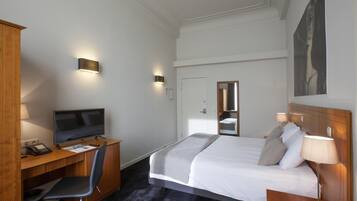 Ein Hotelzimmer mit Bett, Schreibtisch, Stuhl, Fernseher und Nachttischlampen.