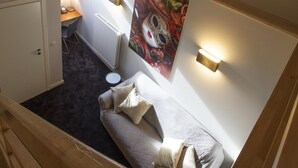 Una habitación de residencia estudiantil con una cama individual, un escritorio, una silla, un radiador y un cuadro colgado en la pared.