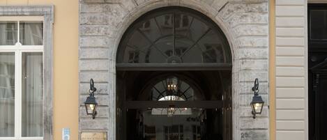 Una entrada de edificio con un arco de piedra, dos ventanas con cortinas y un balcón con barandilla.