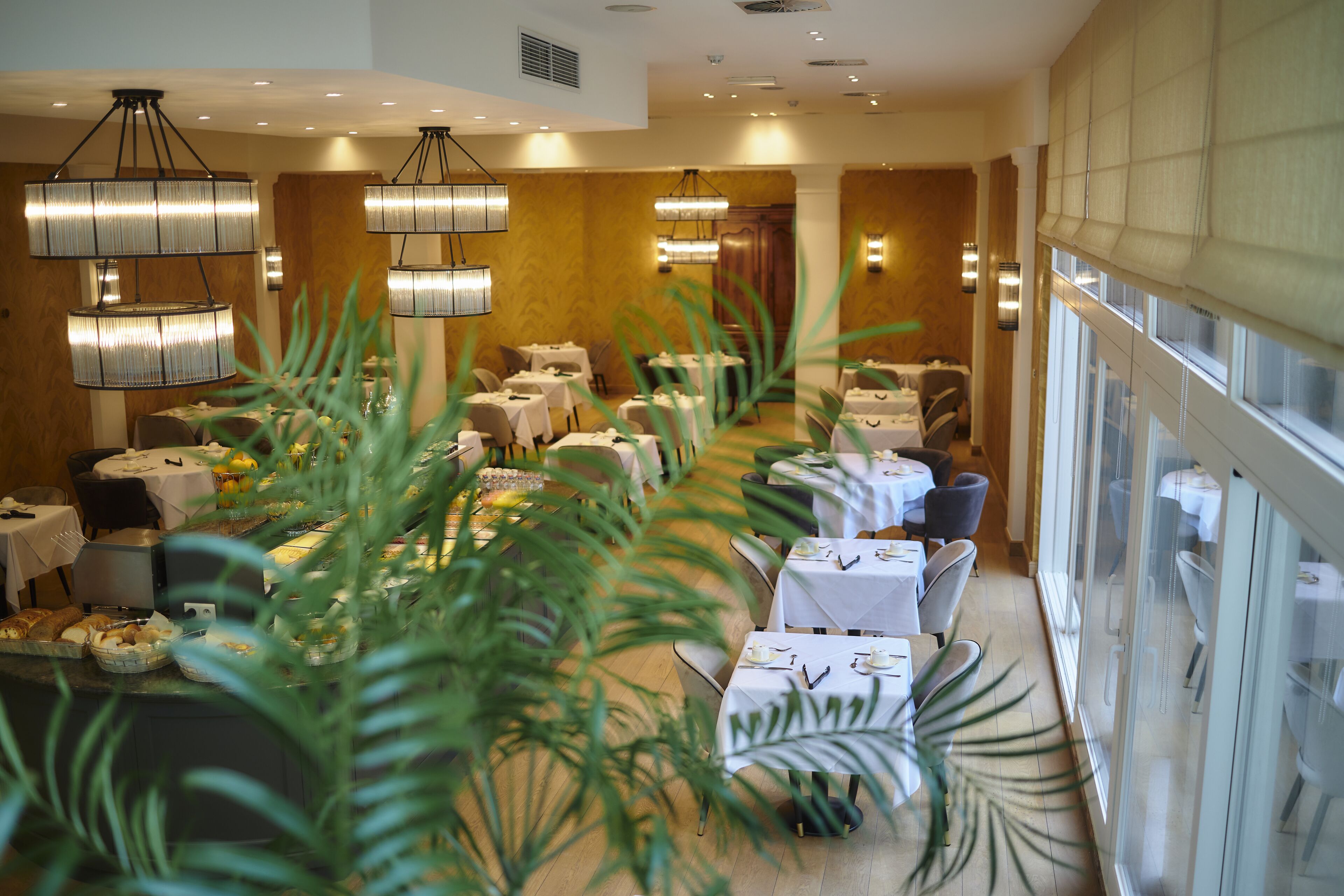A restaurant with multiple tables, hanging chandeliers, and large windows.