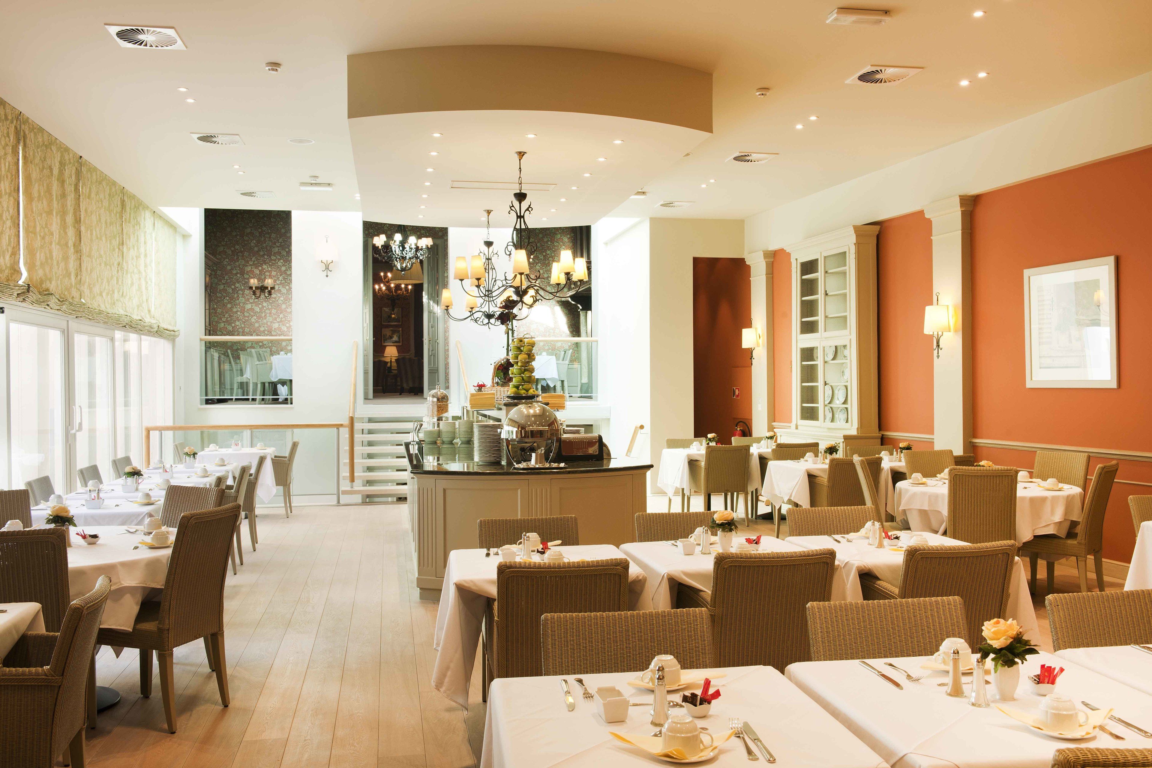 A hotel dining area with multiple tables and chairs, a central bar, and a chandelier.
