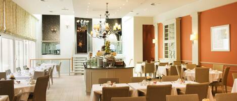 A hotel dining area with multiple tables and chairs, a central bar, and a chandelier.