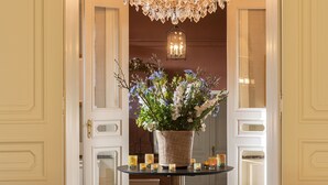 A grand entrance with a chandelier, a floral arrangement, and two brown chairs.