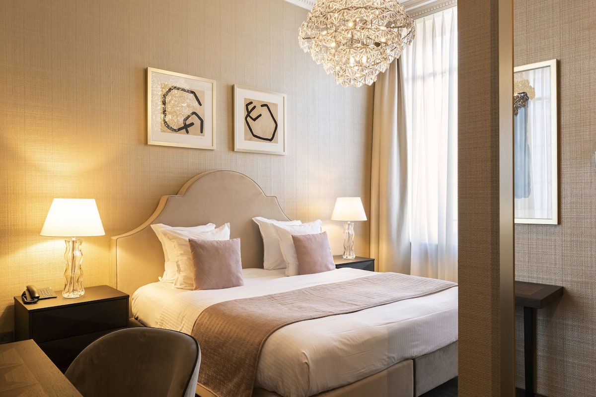 Ein Hotelzimmer mit einem großen Bett, zwei Nachttischen mit Lampen, einem Sessel und einem Bild an der Wand.