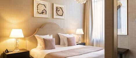 Een hotelkamer met een groot bed, twee nachtkastjes met lampen, een stoel en kunst aan de muur.