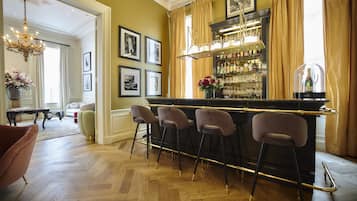 Un espace bar doté d’un parquet en bois à motifs de chevrons, de tabourets de bar, d’un présentoir à verres à vin et d’un lustre.