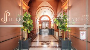 A hotel lobby with a marble floor, a reception desk, and two potted plants.