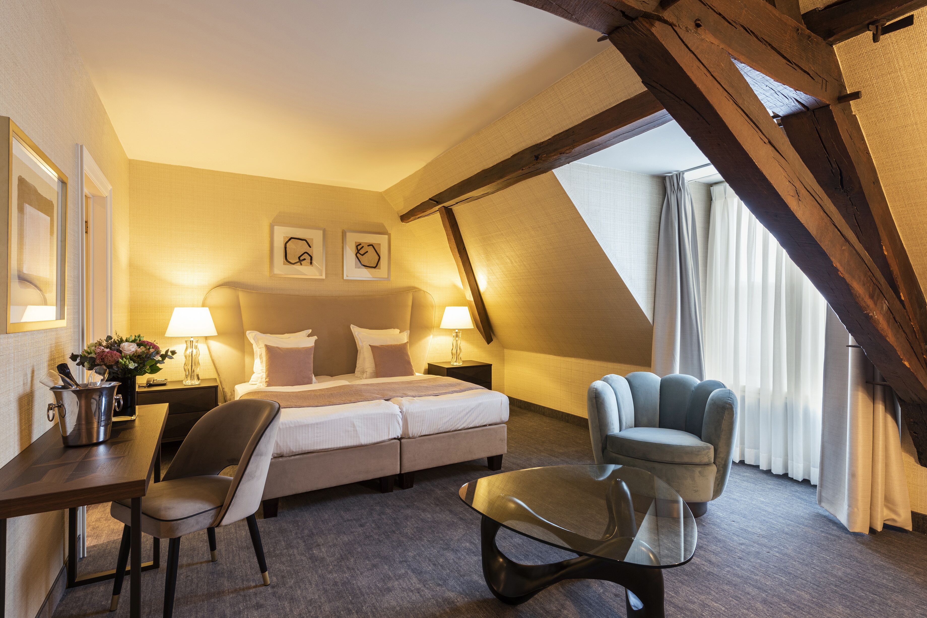 Ein Hotelzimmer mit einem Bett, zwei Nachttischen, einem Sessel und einem Glastisch, mit Blick ins Freie.