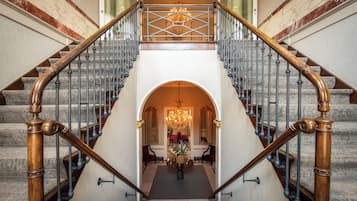 A grand staircase with a chandelier, marble steps, and a floral arrangement at the landing.