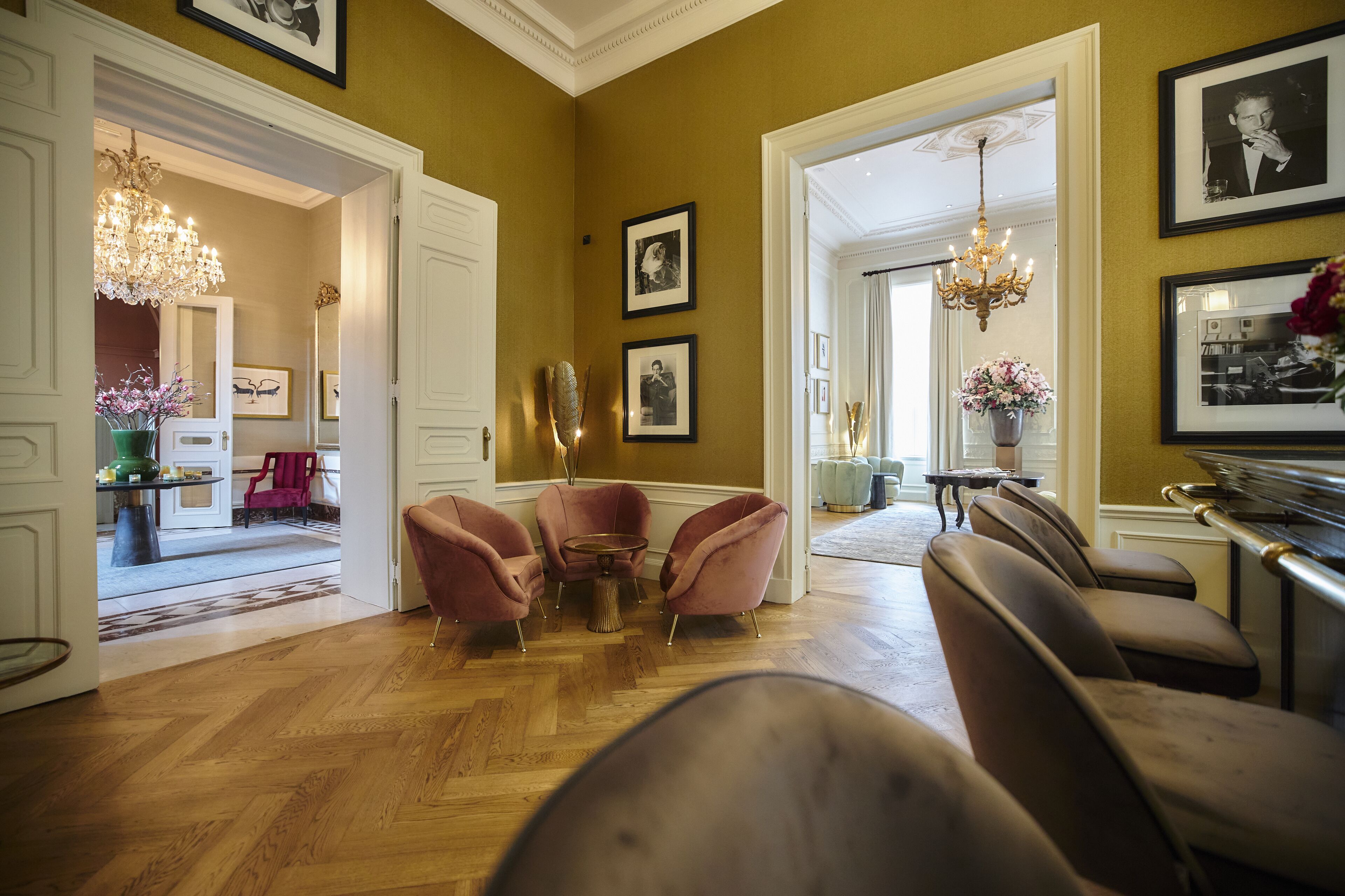 A spacious room with wooden flooring, a chandelier, and a seating area with pink chairs.