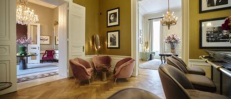 Amplia habitación con suelo de madera, un candelabro y una zona de estar con sillas rosadas.