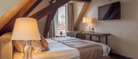 A hotel room with a bed, a desk, a lamp, and a TV.